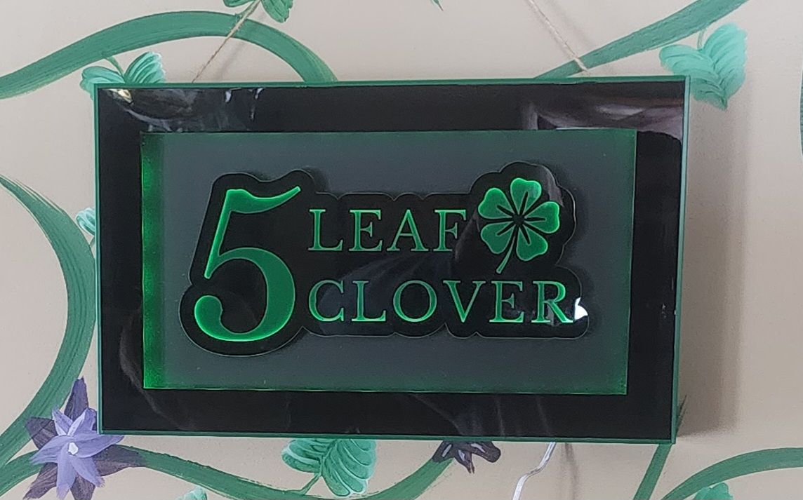 Black plaque with green “5 Leaf Clover” text and a clover symbol on a leafy patterned background