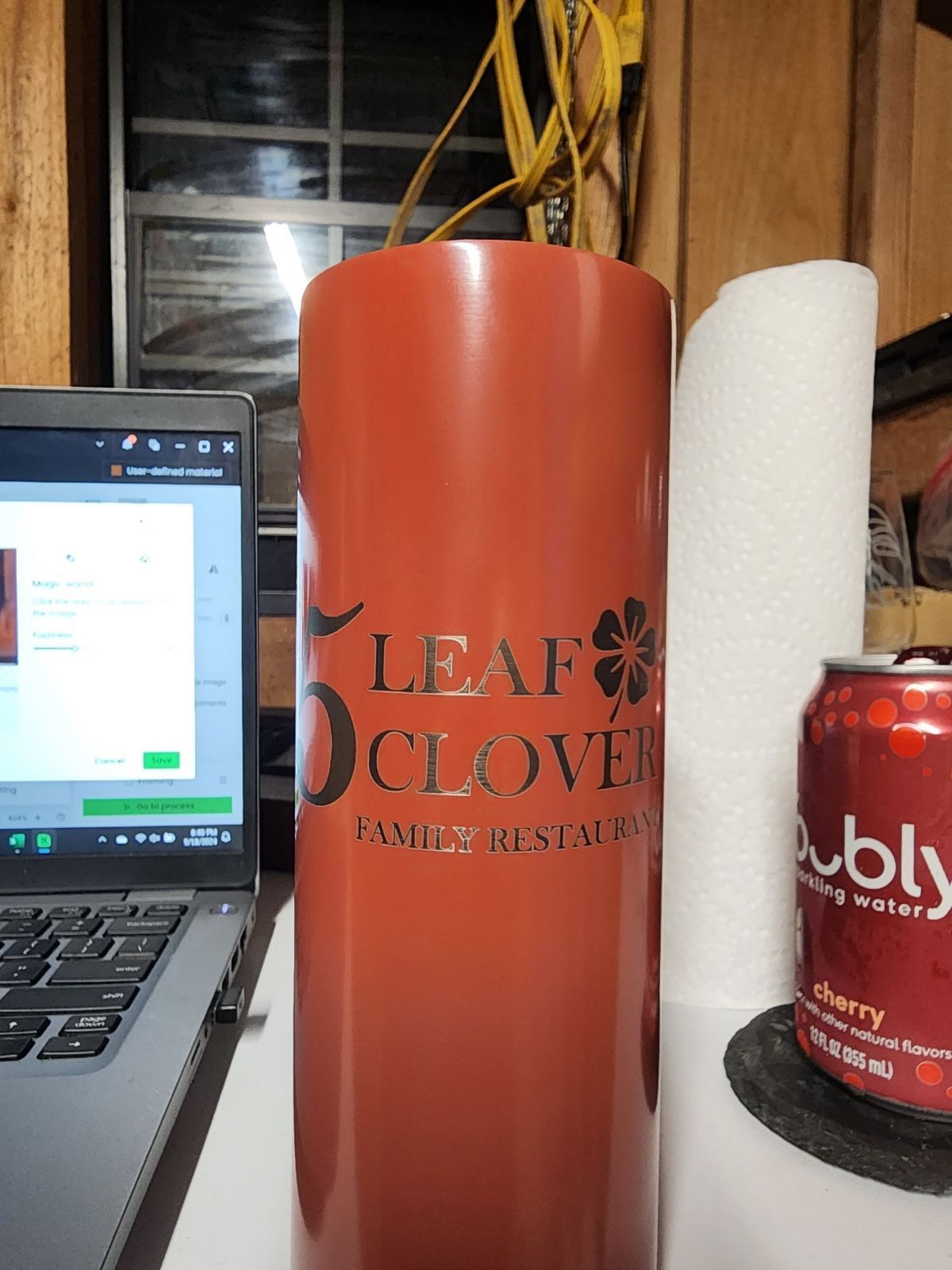 Orange Leaf & Clover cup beside white paper towel roll and laptop on a table