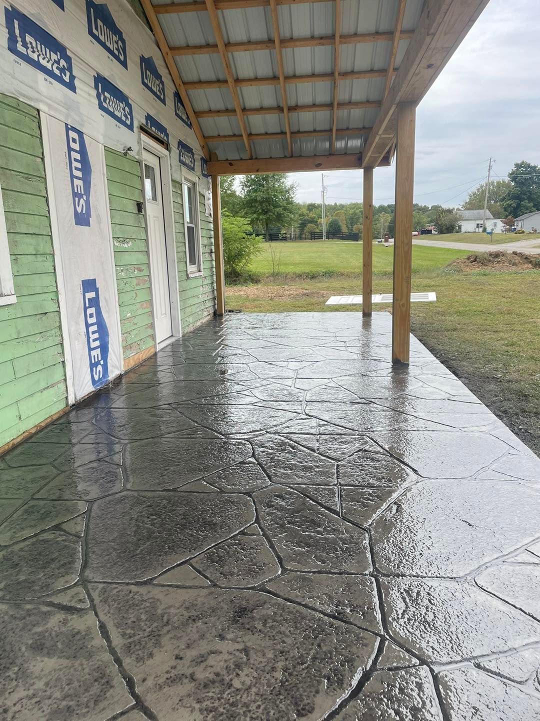 A concrete patio under a covered porch next to a house under construction.
