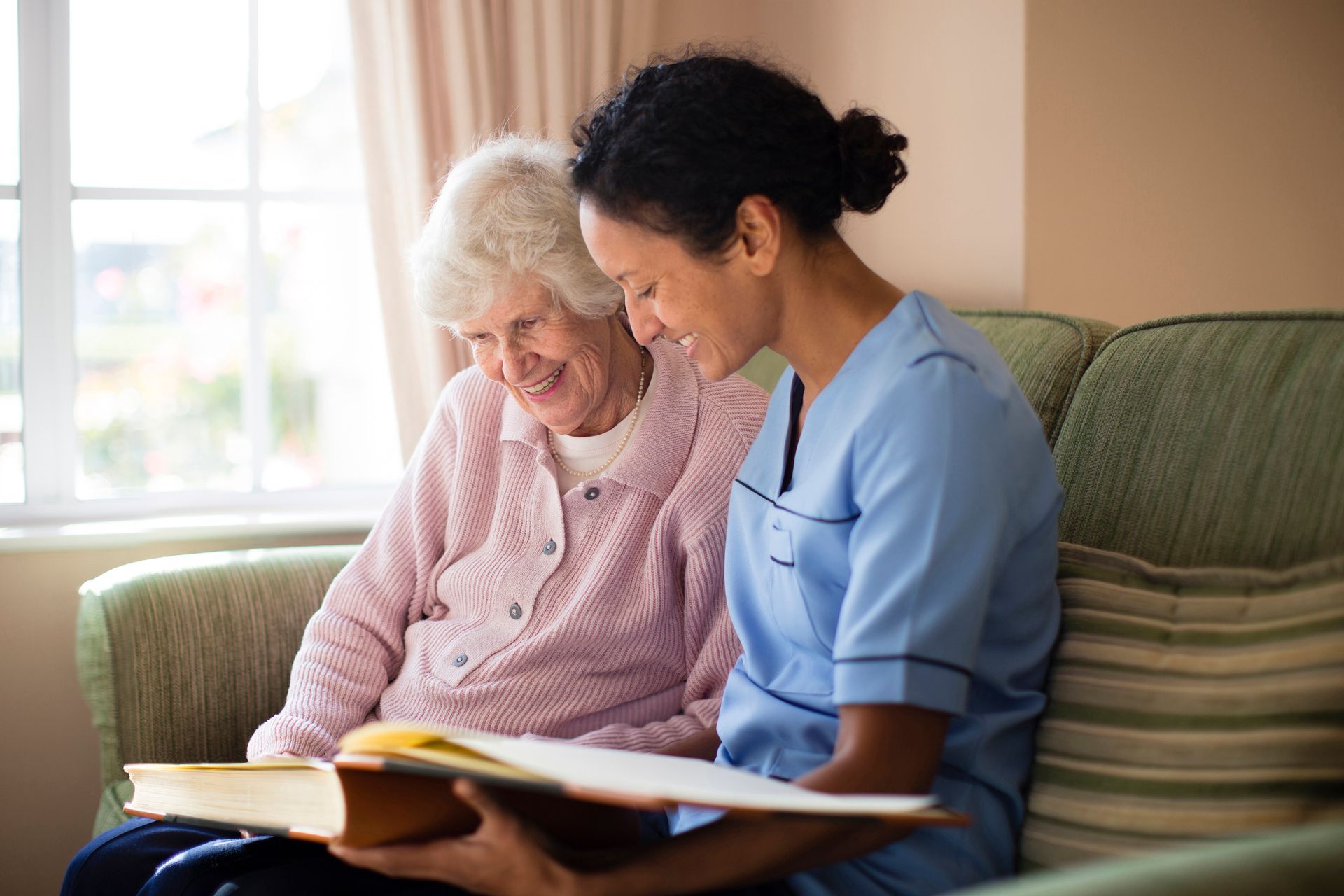 A nurse is helping an elderly woman read a book.