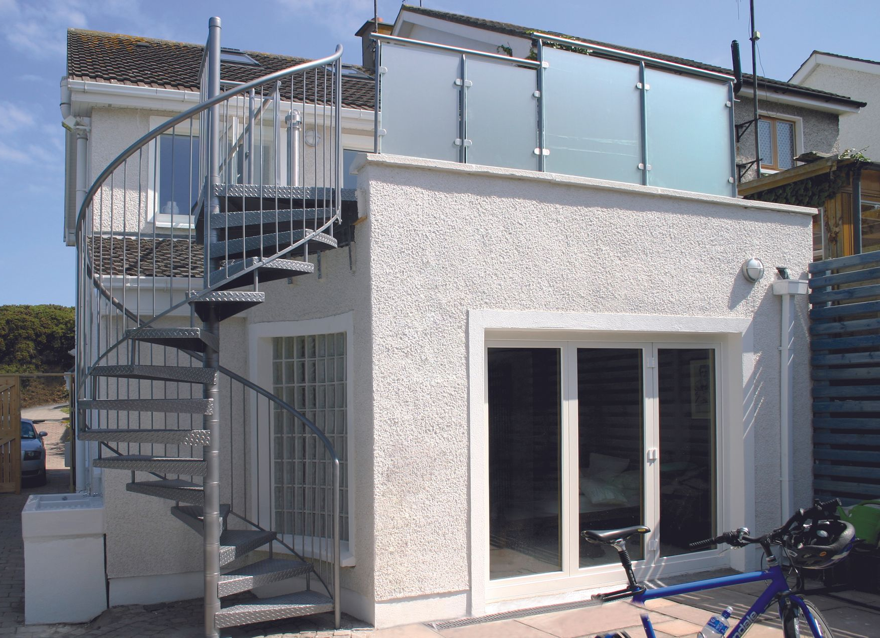 Casa moderna bianca con terrazza sul tetto e scala a chiocciola esterna.