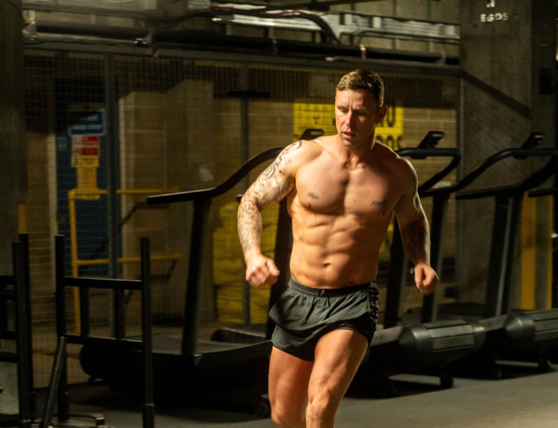 A shirtless man is running on a treadmill in a gym.