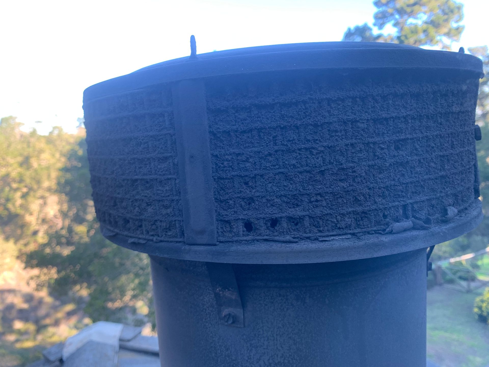 A close up of a chimney on a roof with trees in the background.