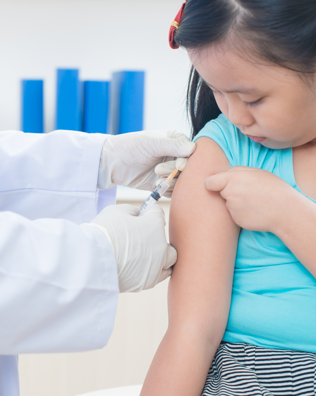 Doctor giving a shot to a girl. She is looking down at her arm where the shot is going.