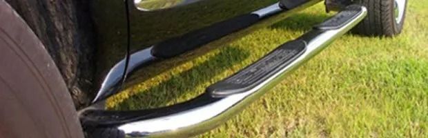 Black vehicle side step with chrome trim beside a grassy lawn