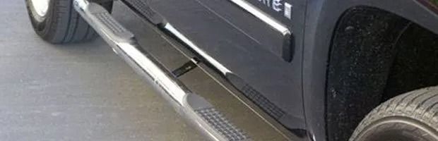 Close-up of a black pickup truck’s side step and front wheel on a road.