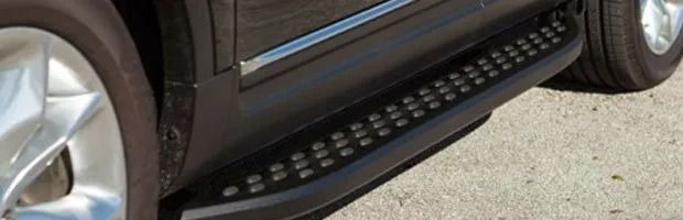 Close-up of a black SUV’s side step and front wheel on a paved surface.