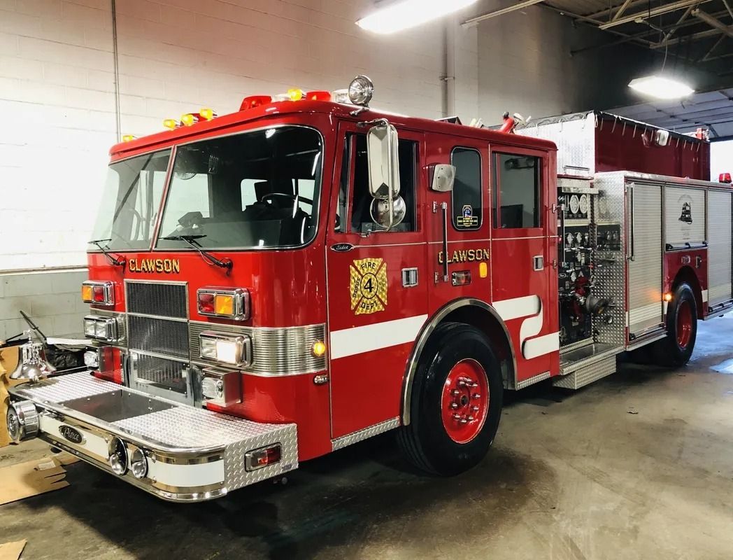 Red fire truck parked indoors in a garage, viewed from the front left side.