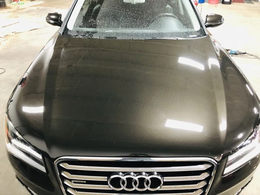 Black Audi sedan seen from the front in a garage, with a dusty hood and grille.