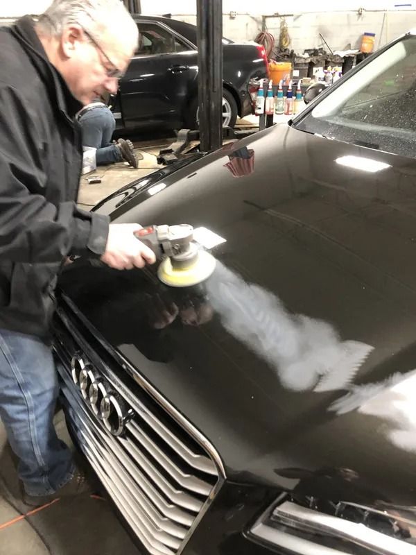 Man polishing the hood of a black car in an auto shop with a buffer tool