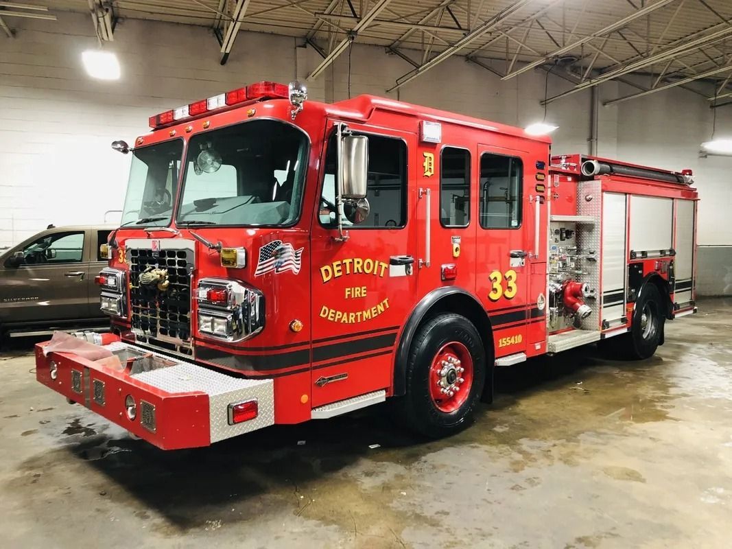 Red fire truck parked indoors in a garage, bright red with white trim and emergency lights.