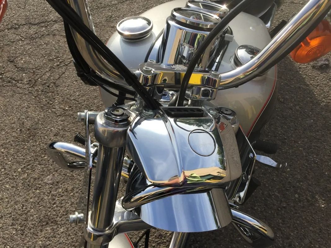 Chrome motorcycle fuel tank and handlebars parked on pavement, with black cables and an orange turn signal.