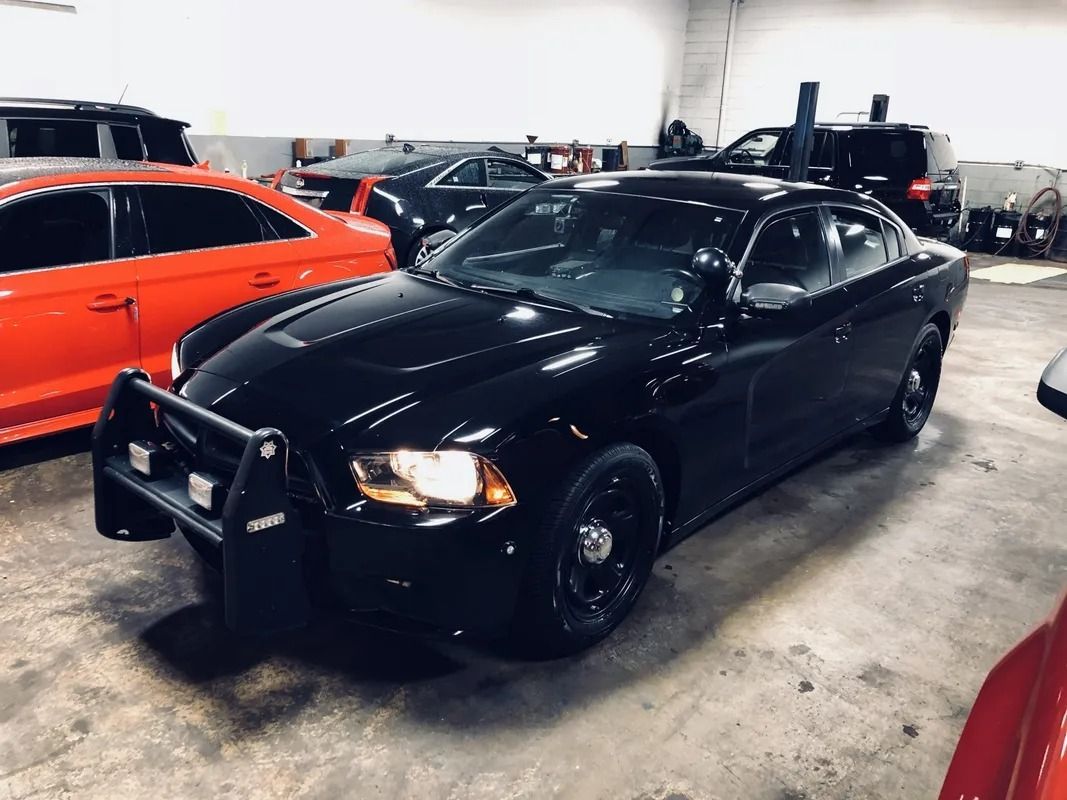 Black police sedan parked indoors, with an orange car beside it and other vehicles in the background