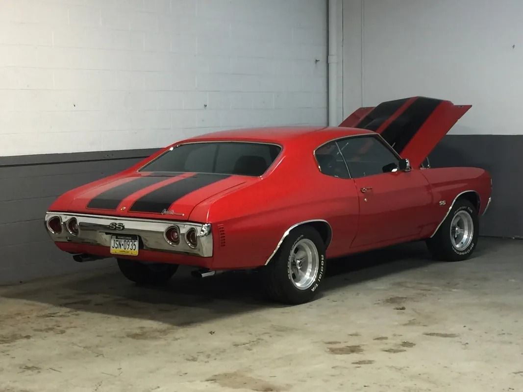 Red classic muscle car with hood open, parked indoors on a concrete floor.