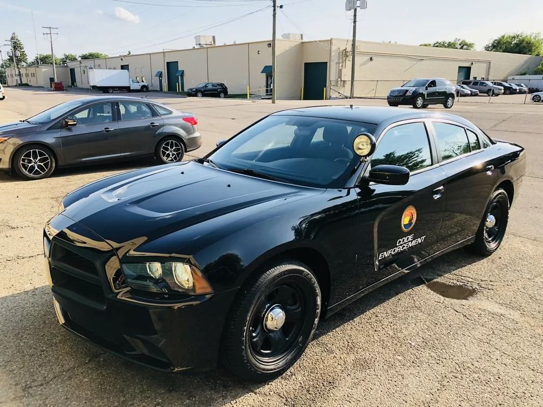 Black Dodge Charger parked in a lot, with police-style decals and a building in the background