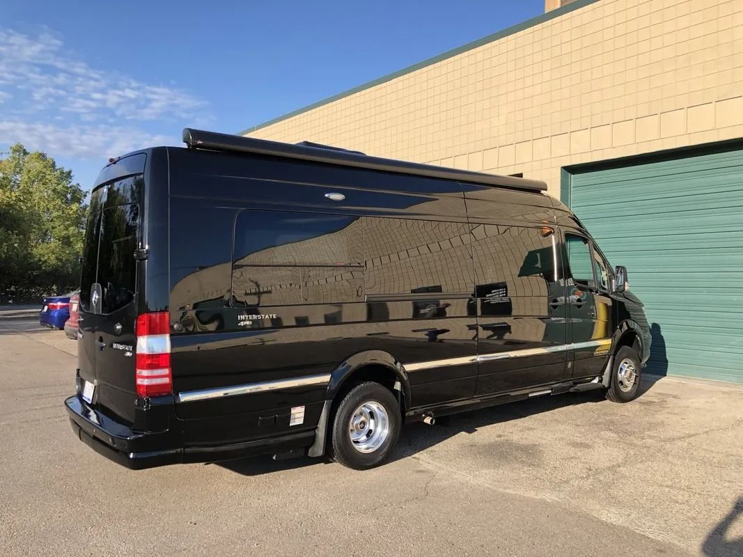 Black cargo van parked beside a beige industrial building in sunlight