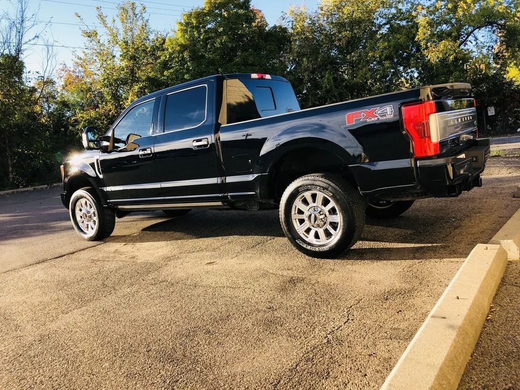 Black pickup truck parked on pavement beside a curb with trees in the background