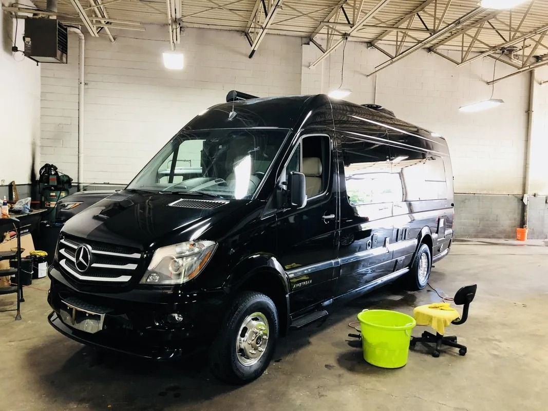 Black Mercedes van inside a garage with yellow cleaning buckets and tools nearby
