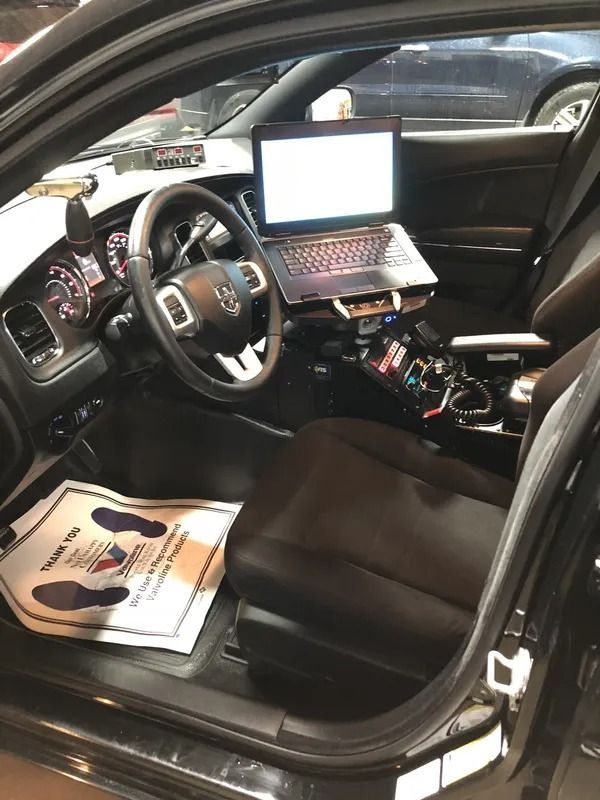 Car interior with steering wheel, laptop on passenger seat, and paperwork on the floorboard.