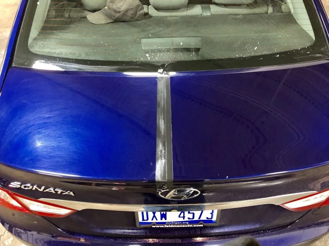 Blue sedan hood with silver stripe, viewed from the rear, showing a license plate.