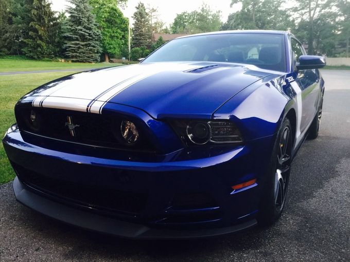 Blue Ford Mustang with white racing stripes parked on a driveway outdoors
