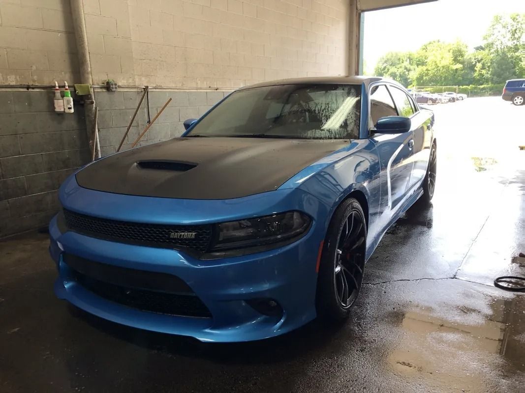 Blue sports car parked in a car wash bay, wet from cleaning, with sunlight outside.