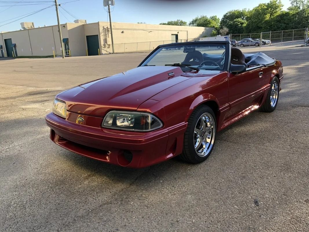Maroon convertible sports car parked on a sunlit industrial lot