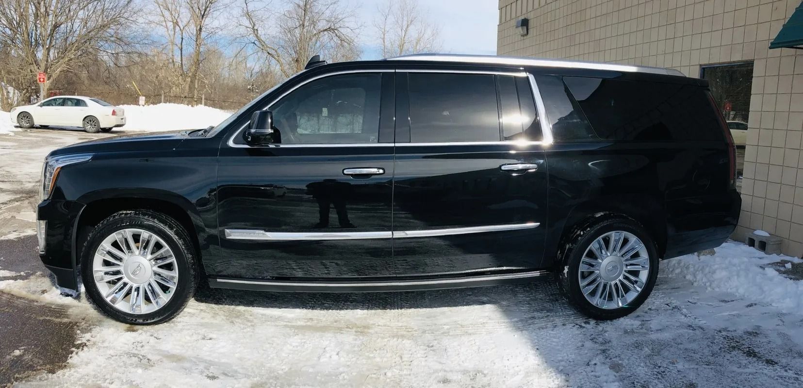 Black SUV parked on a snowy lot beside a building in daylight