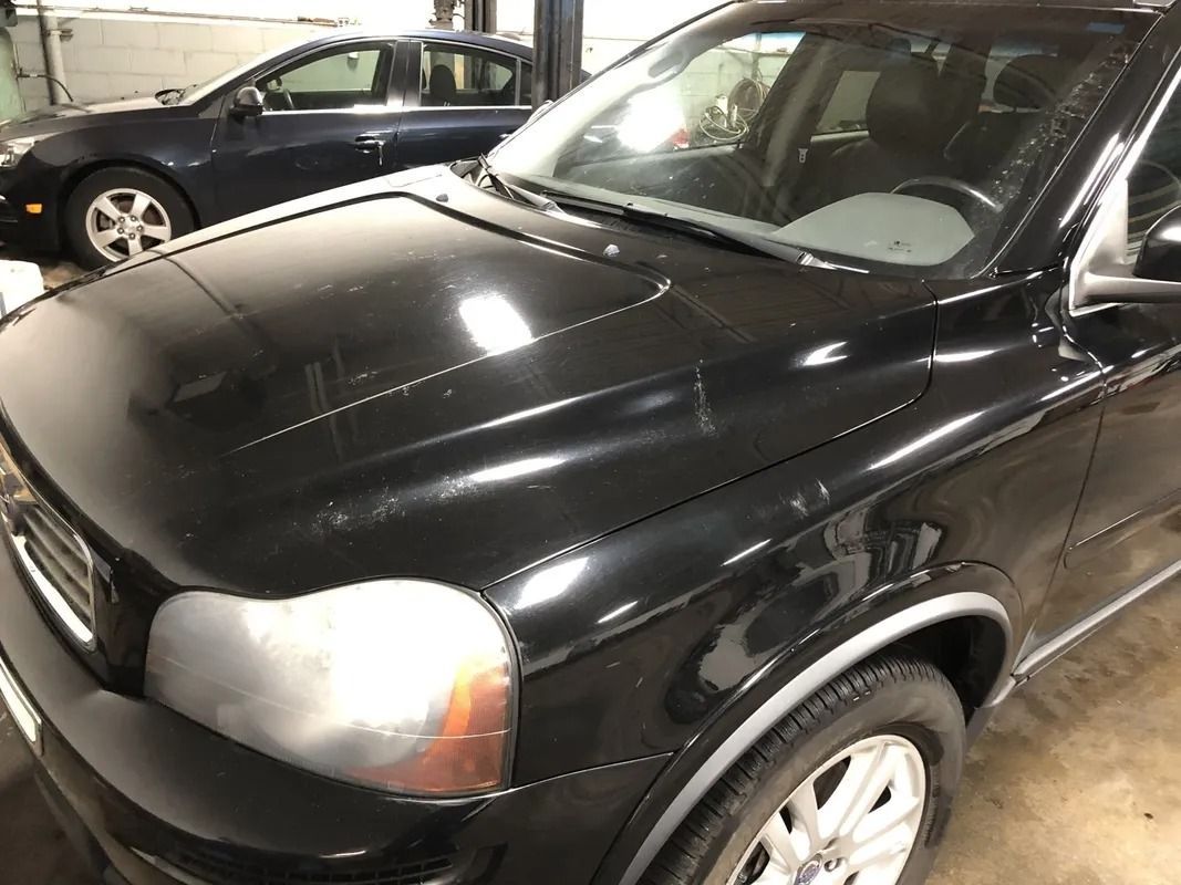 Black SUV parked indoors next to a dark sedan, showing the front and hood.