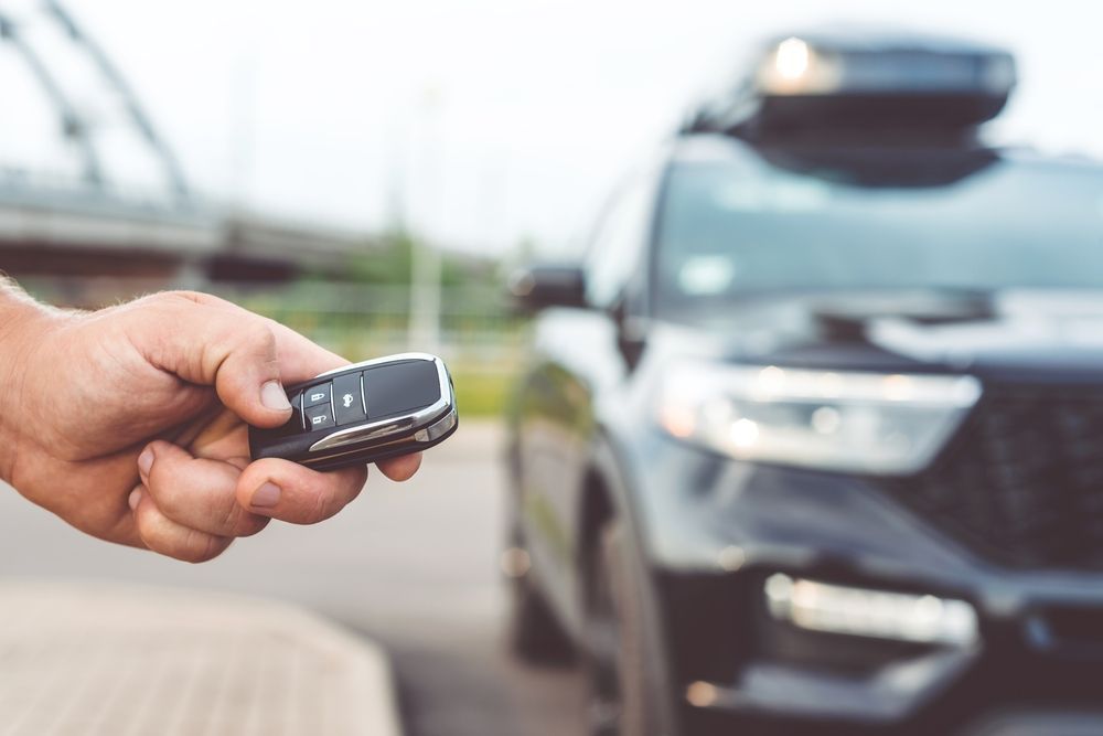 Hand holding a car key fob near a black SUV in a parking lot
