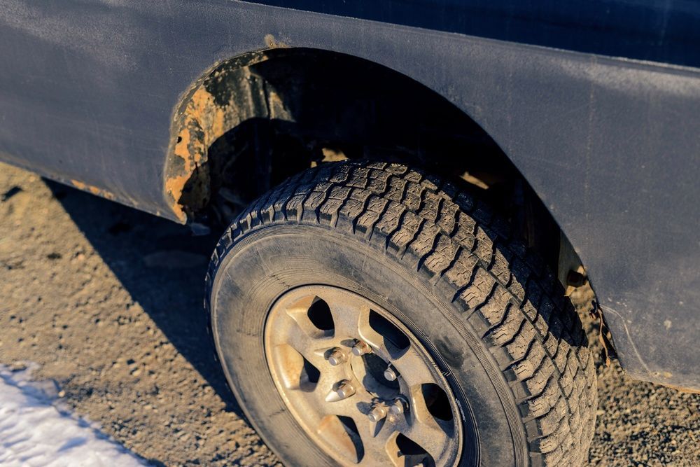 Muddy wheel and tire on a dark vehicle with rust around the wheel well