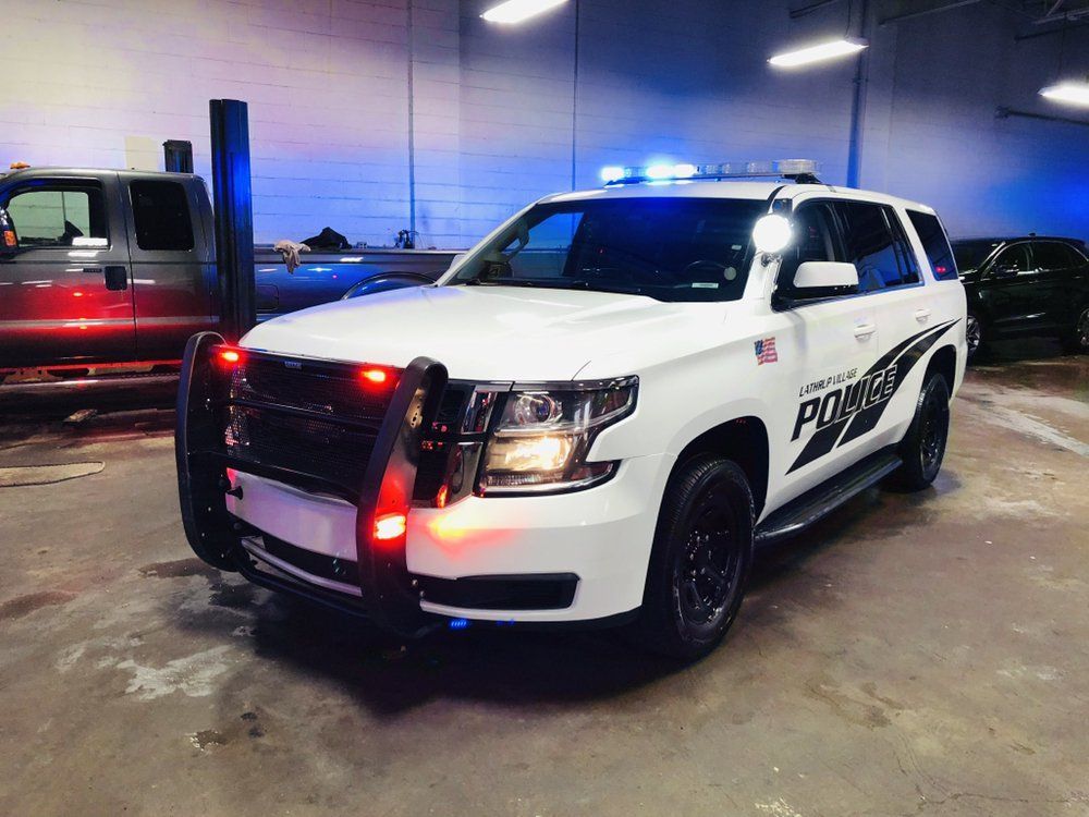White police SUV with flashing lights parked inside a garage with other vehicles nearby