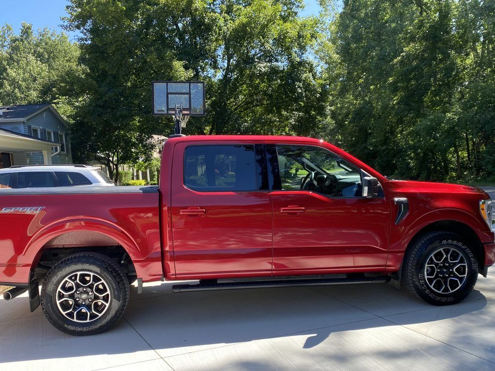 Red pickup truck parked in a driveway with trees and a basketball hoop in the background