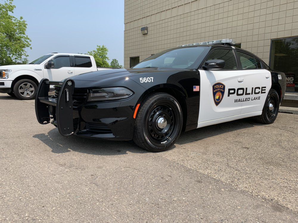Black-and-white police cruiser parked outside a beige building on a sunny day