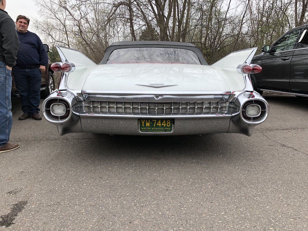 Front view of a white classic Cadillac with tail fins, parked on a street with people standing nearby.