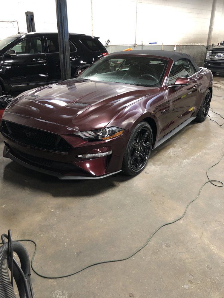 Maroon convertible sports car parked indoors in a garage, with a black SUV beside it