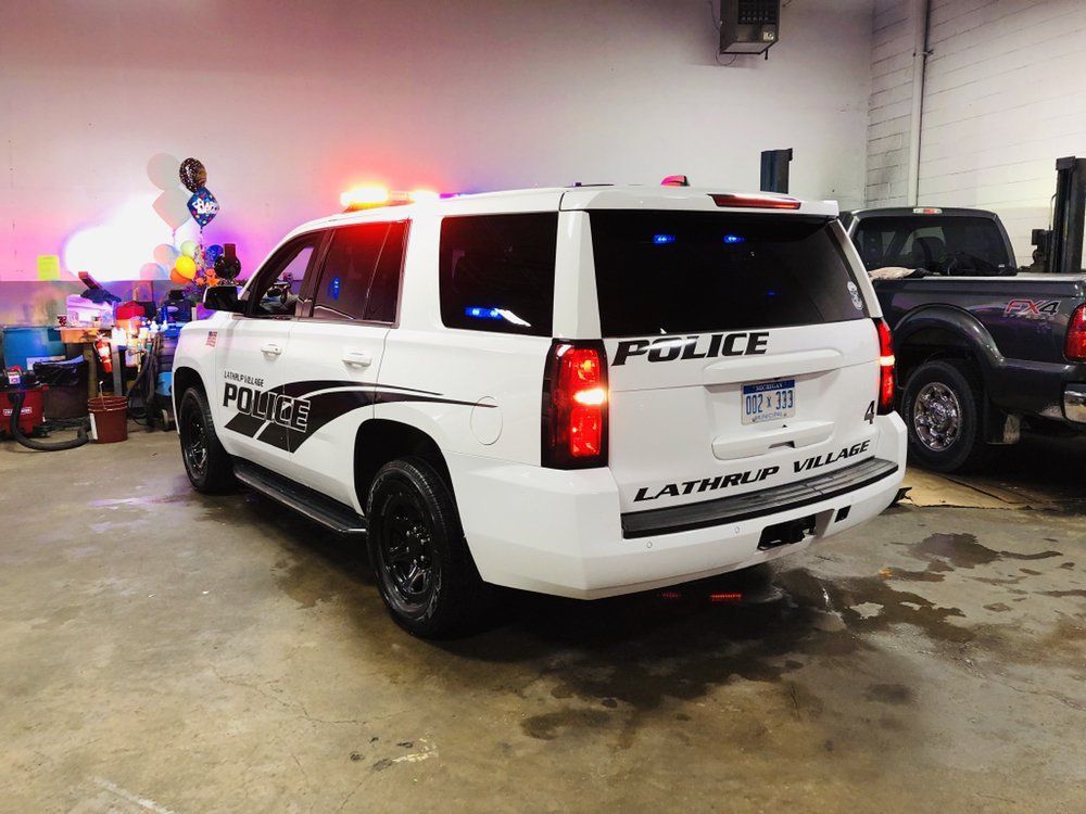 White police SUV with flashing lights parked indoors beside other vehicles, rear view
