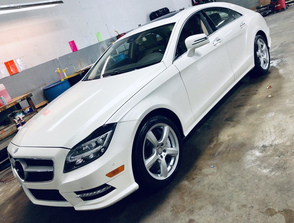 White sedan parked in a garage, angled front-left view on a wet floor.