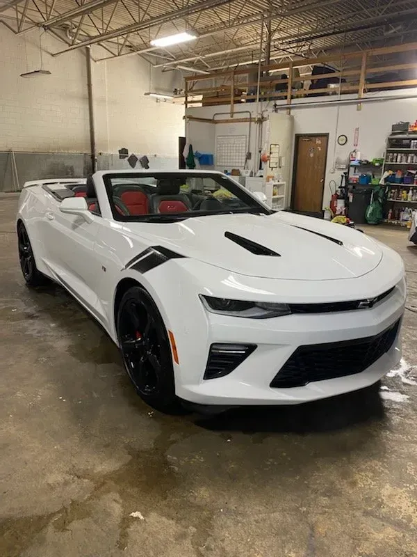 White Chevrolet Camaro parked indoors in a garage, seen from the front-left side.