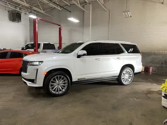 White SUV parked in an auto shop garage beside a red car and a lift