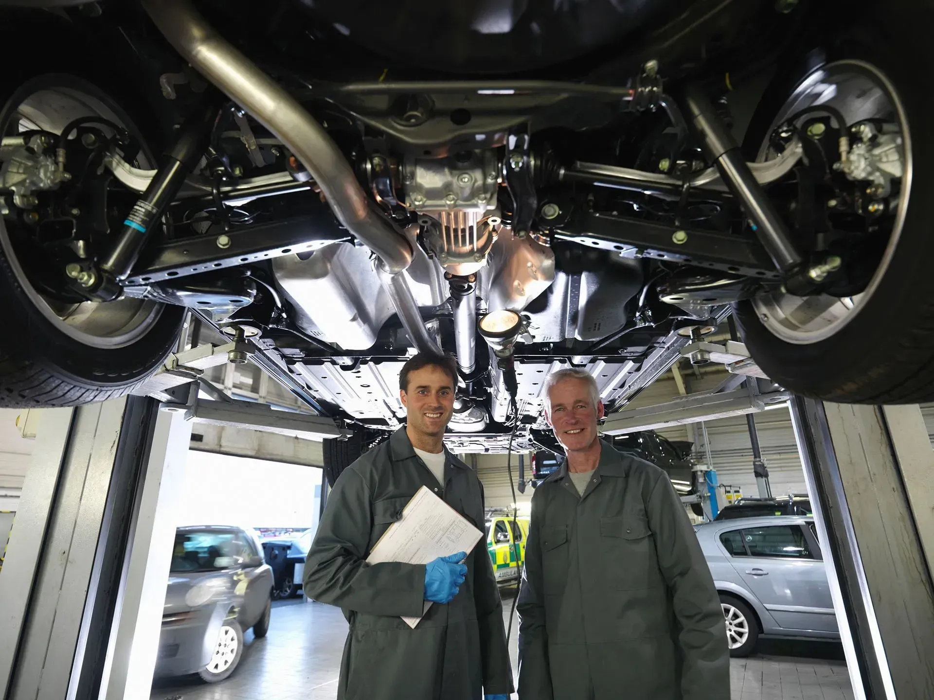 Two mechanics standing under a car on a lift in an auto repair shop