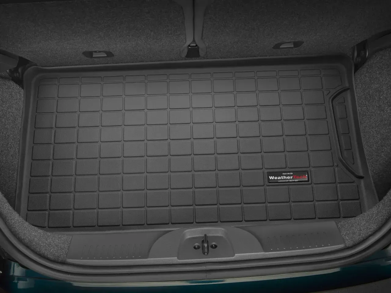 Car trunk with a black quilted cargo mat and small storage tray, viewed from the rear.