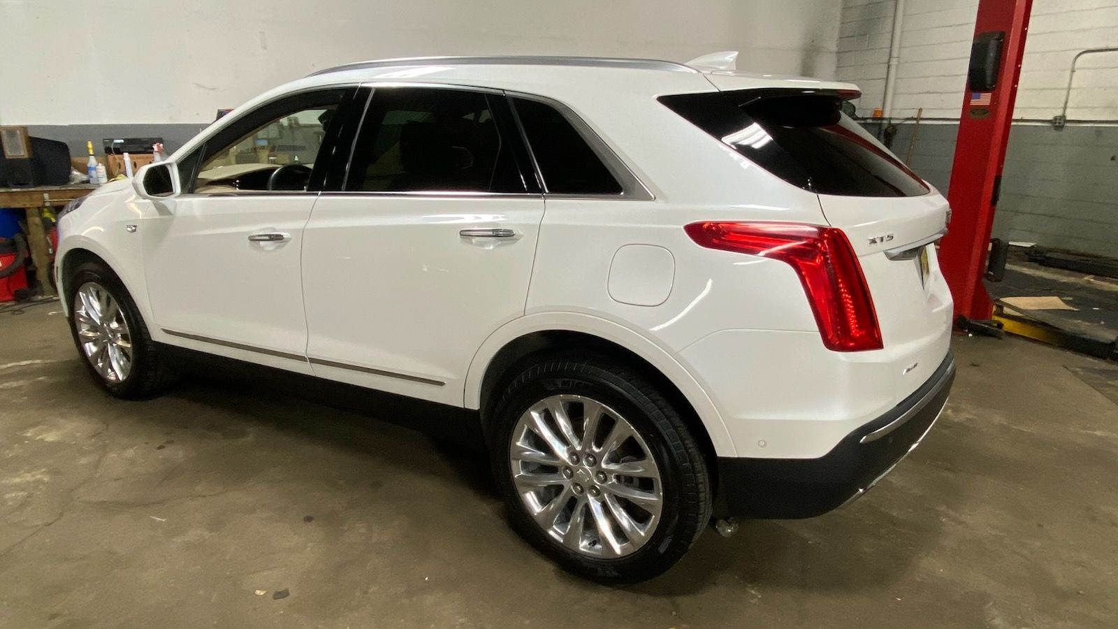 White SUV parked indoors in a garage, side view with chrome wheels and red rear taillight accents