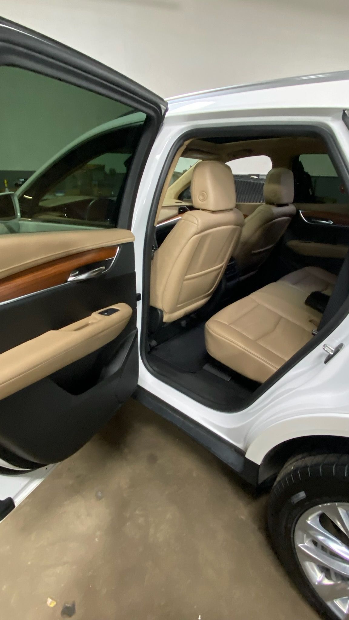 Open rear passenger door of a white SUV, showing beige leather seats and wood trim.