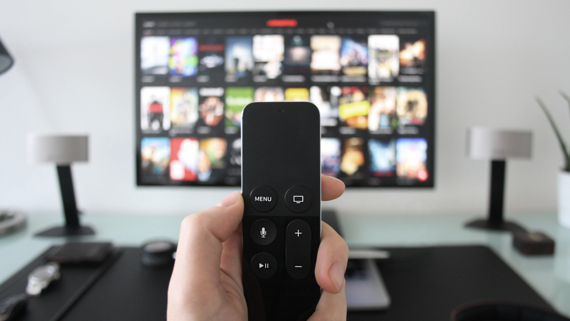 A person is holding a remote control in front of a television.