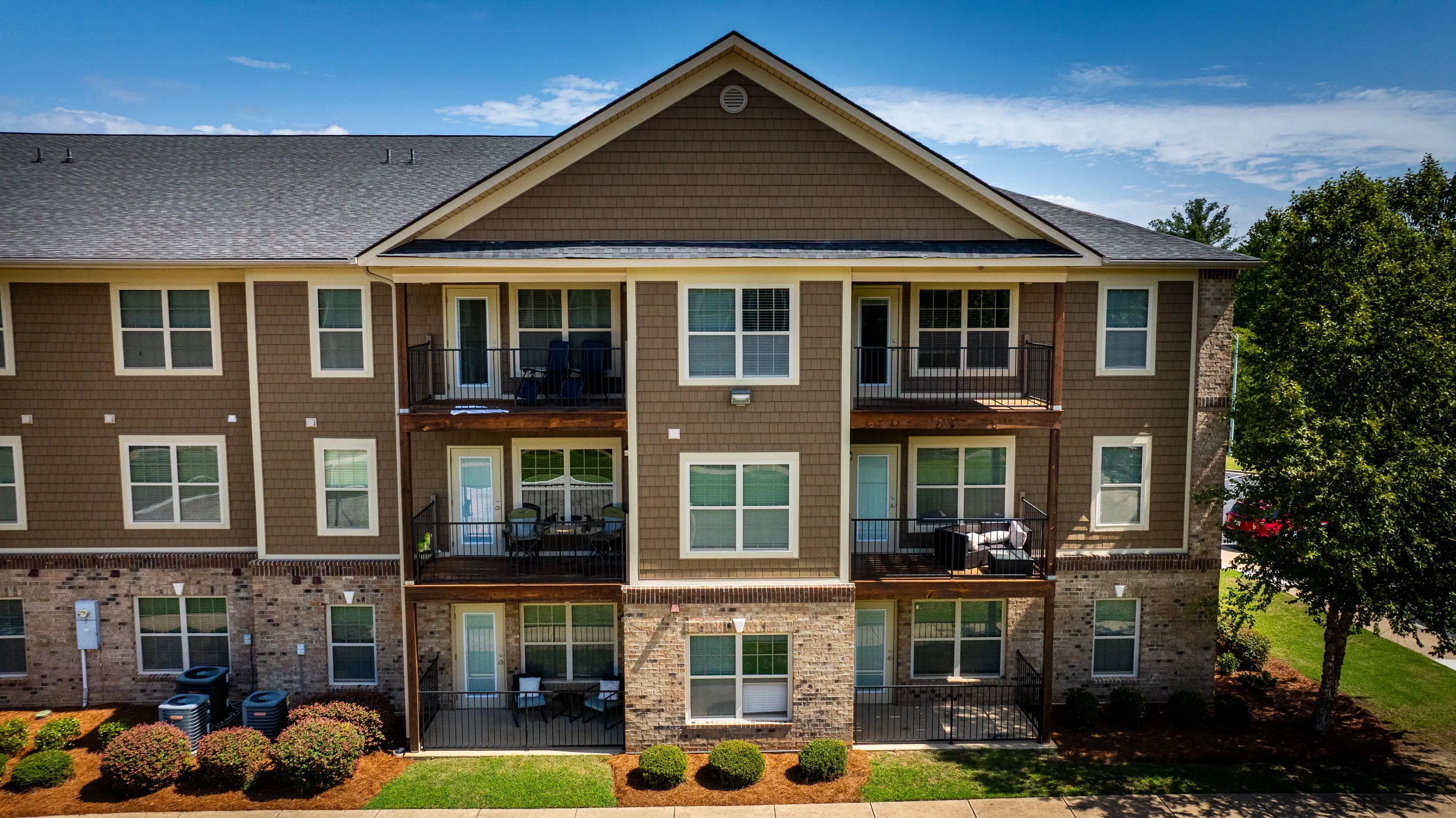 Exterior of a three-story apartment building with brown siding and brick base.
