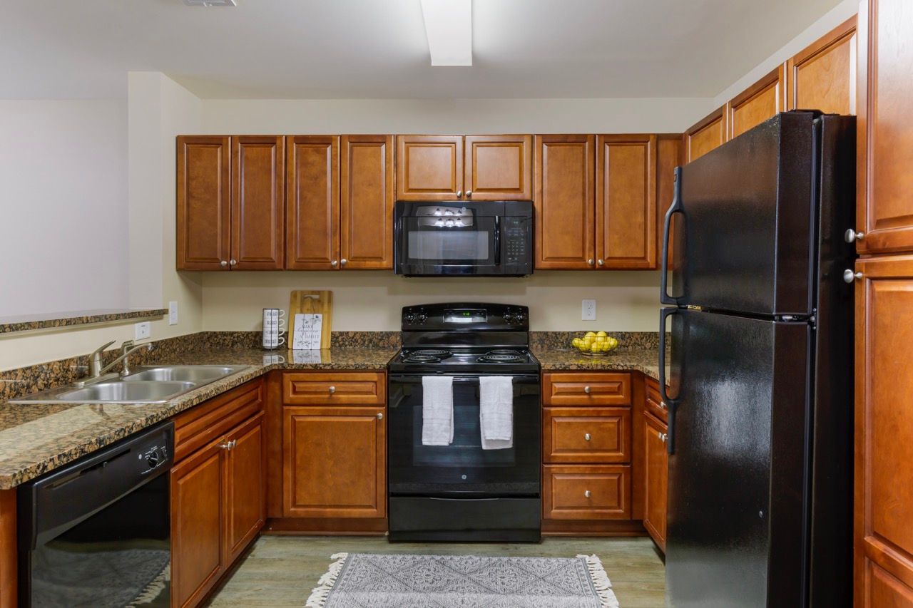 Apartment kitchen with brown wooden cabinets, black stove, microwave, fridge, and granite countertops.