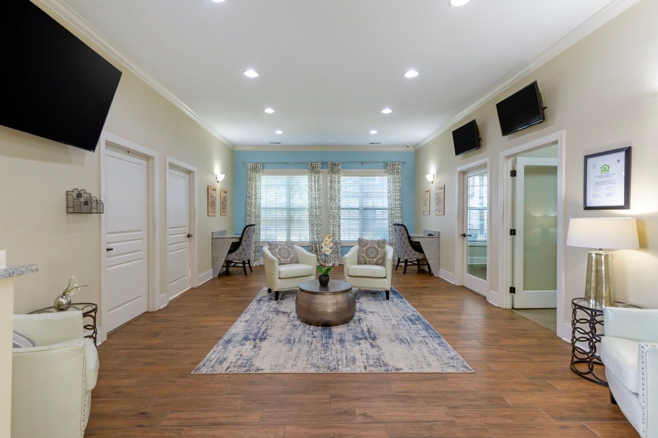 Bright community lounge with cream seating, a round coffee table, and wall-mounted TVs.