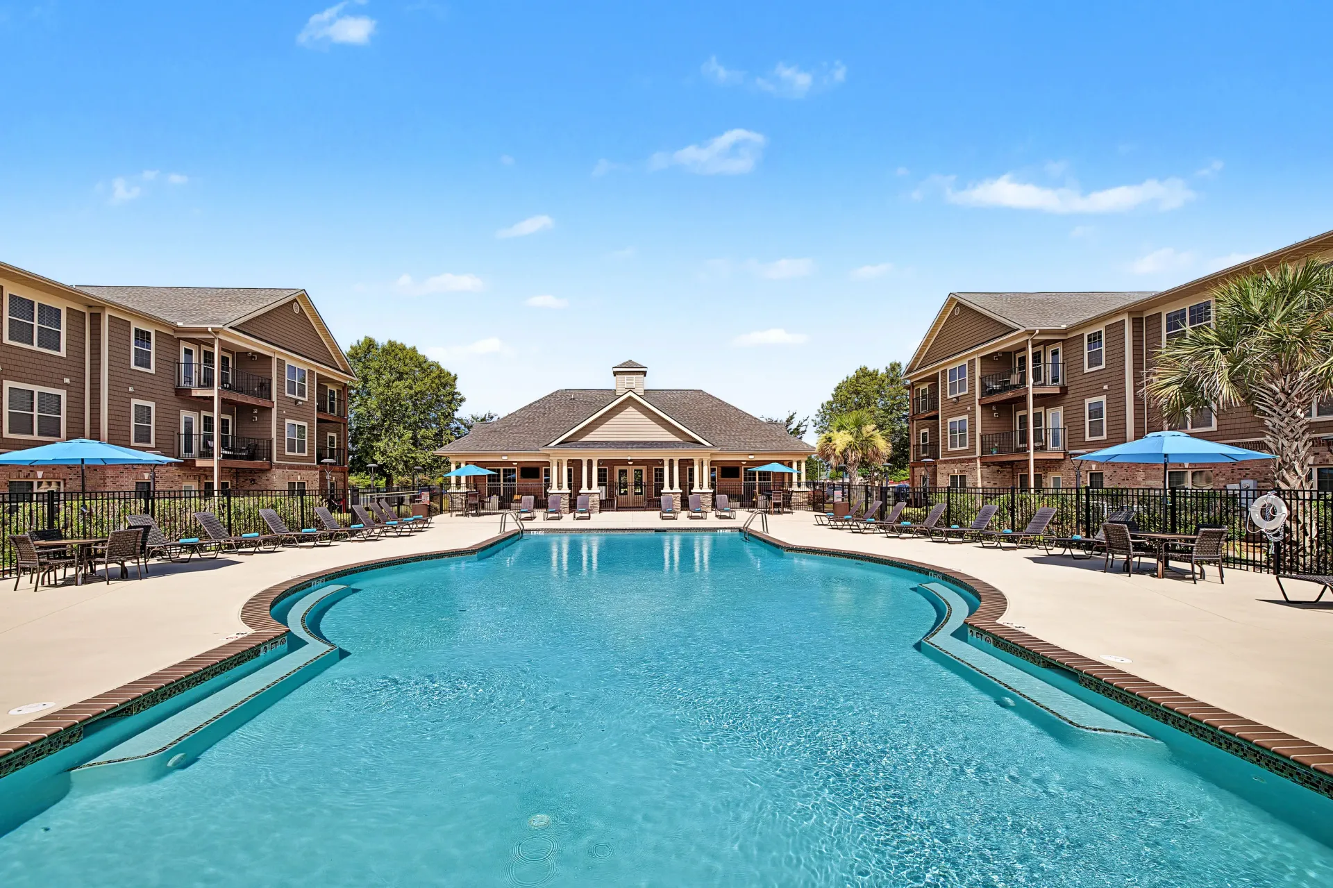 Large swimming pool with lounge chairs and umbrellas, surrounded by apartment buildings.