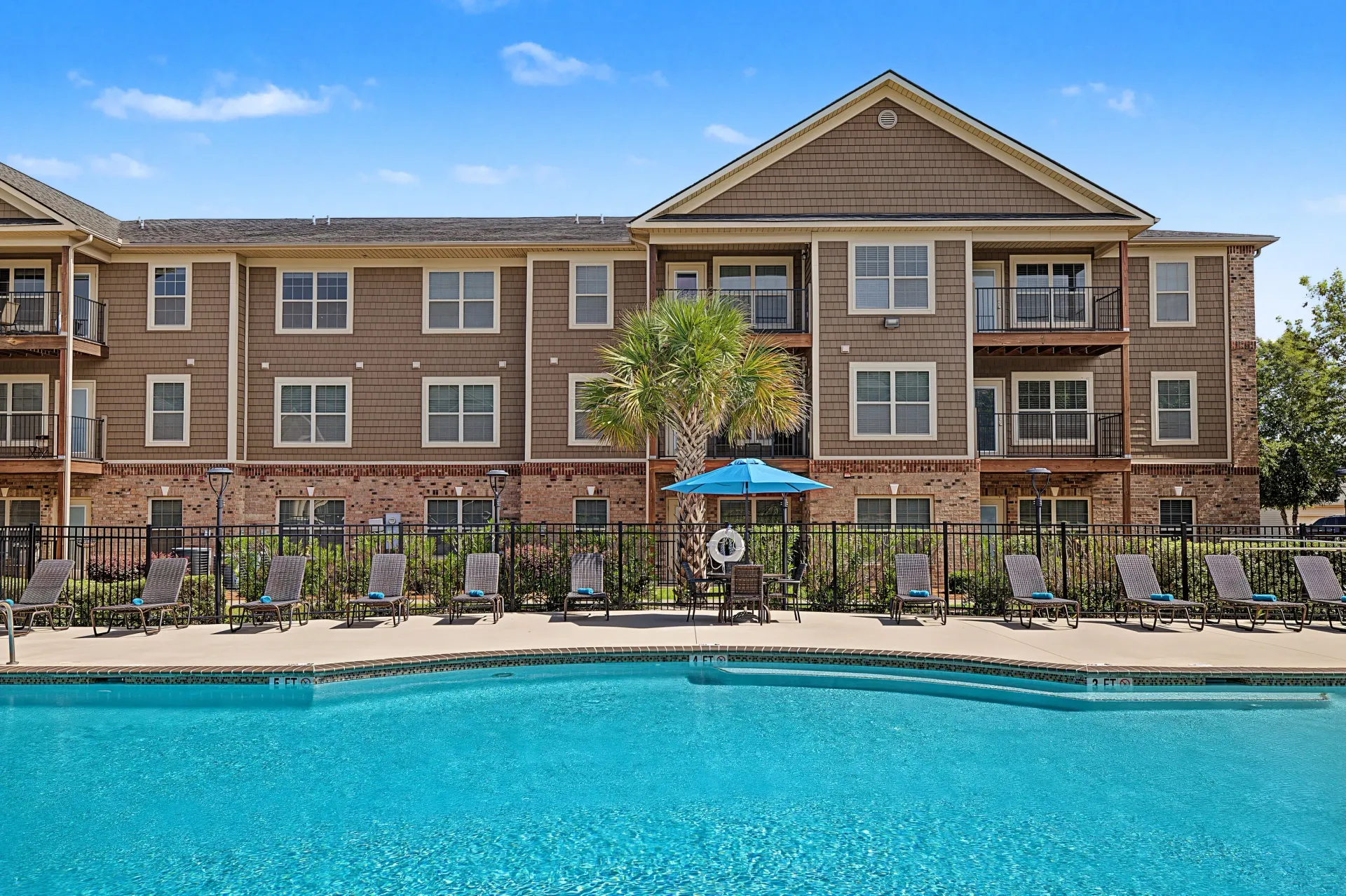 Outdoor swimming pool with lounge chairs and a resort-style apartment building in the background.